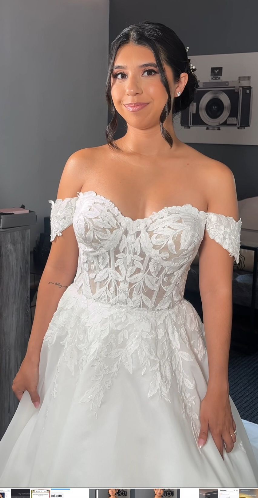 Woman in an off-shoulder lace wedding dress with floral patterns, standing indoors.