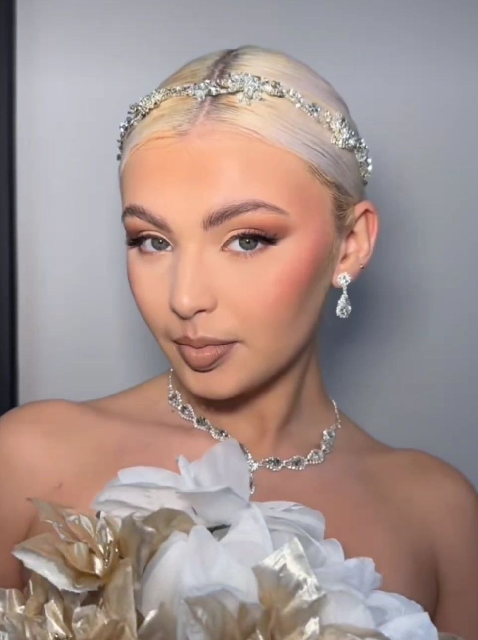 Person with ornate headband and jewelry, wearing a strapless outfit adorned with flowers.